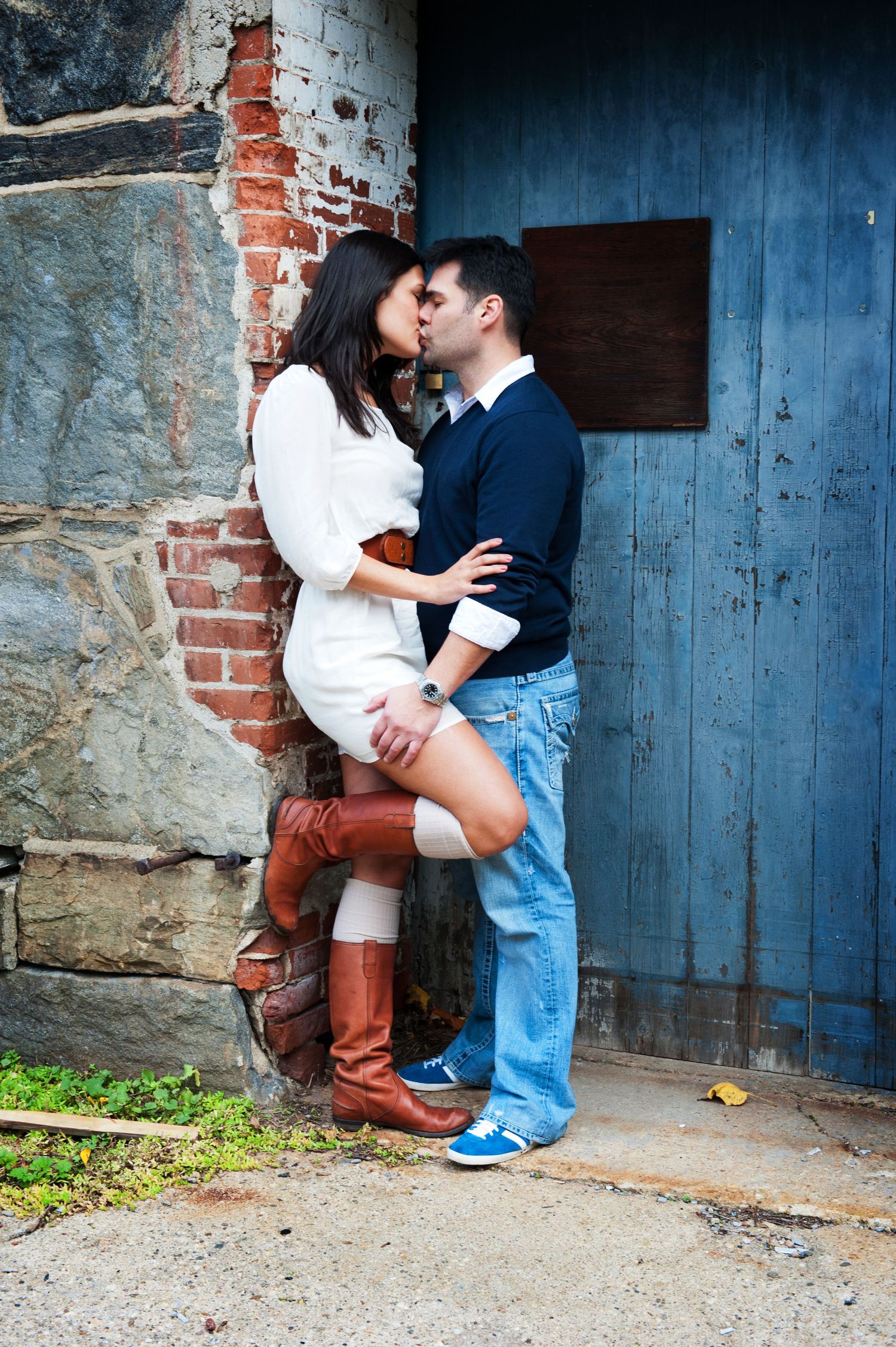 A couple embraces against a rustic blue door and brick wall creating an intimate engagement photo.