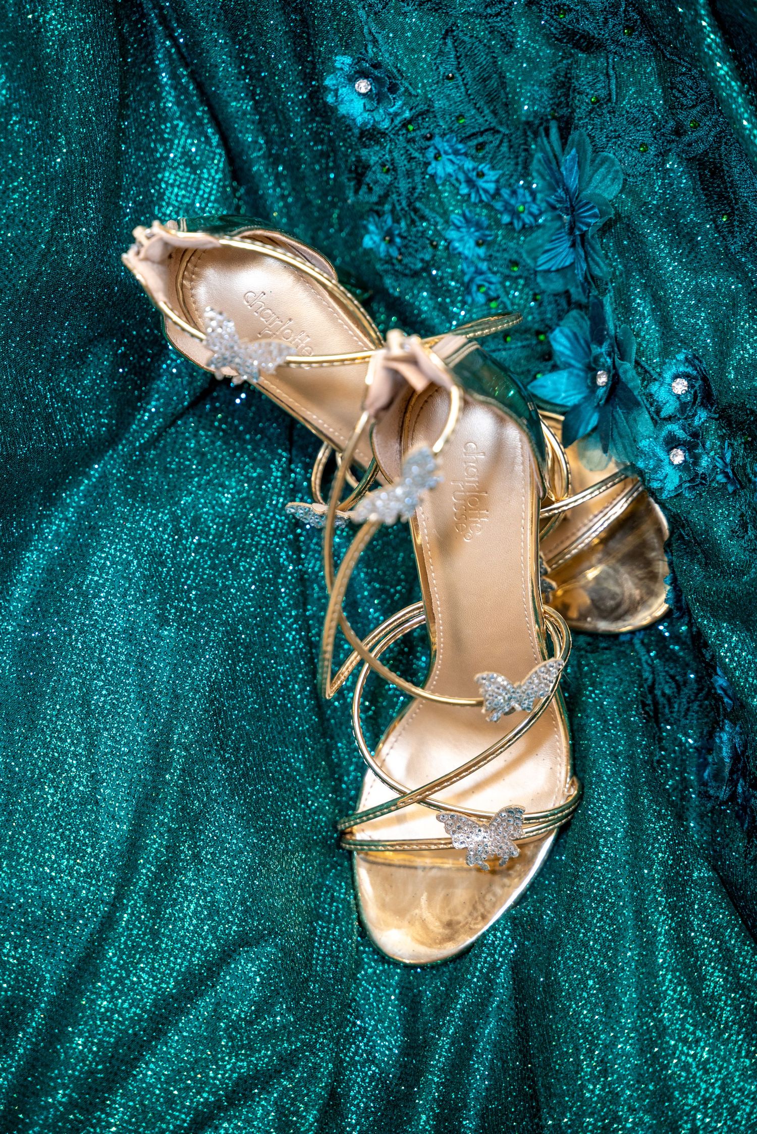 Gold metallic high heel sandals arranged on teal sparkly fabric.