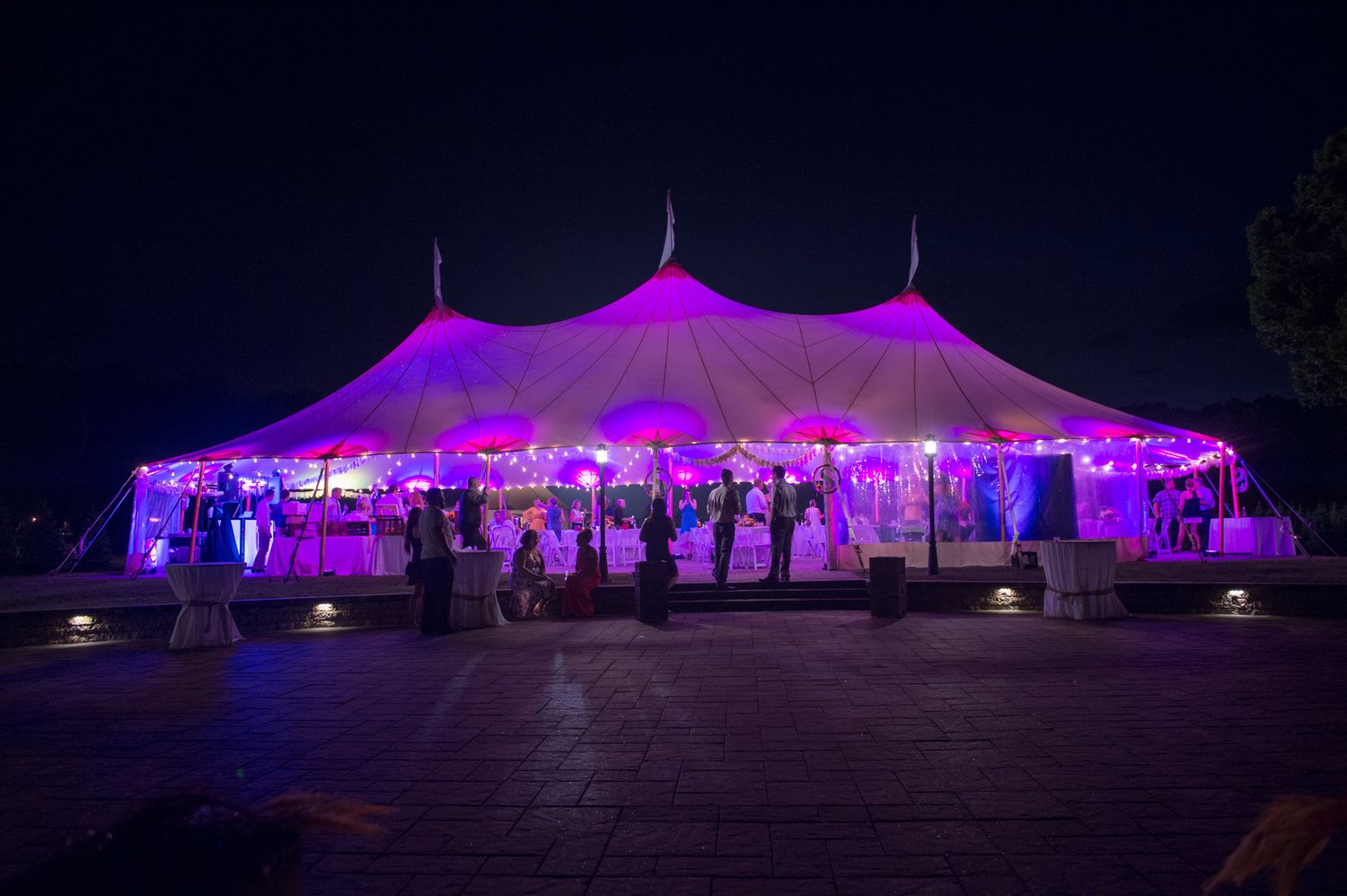 Large white wedding tent illuminated with purple lighting at night creating magical atmosphere.