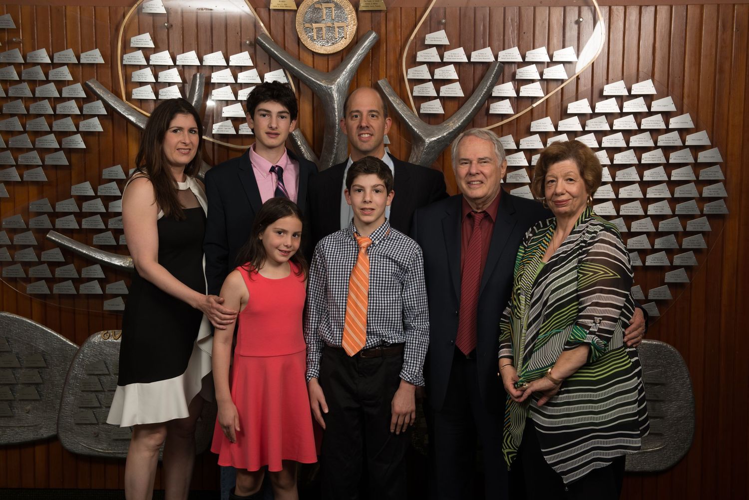 Group photo taken in front of a decorative wooden wall at a formal event.