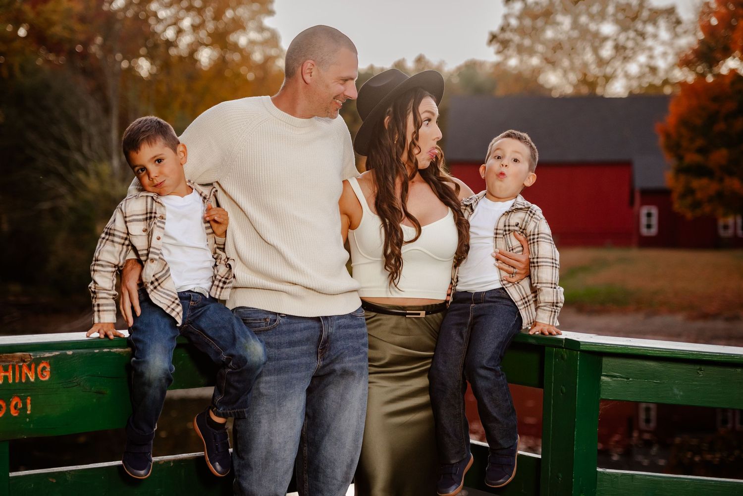 A group relaxes on a green bench surrounded by fall trees and a red barn in the distance.
