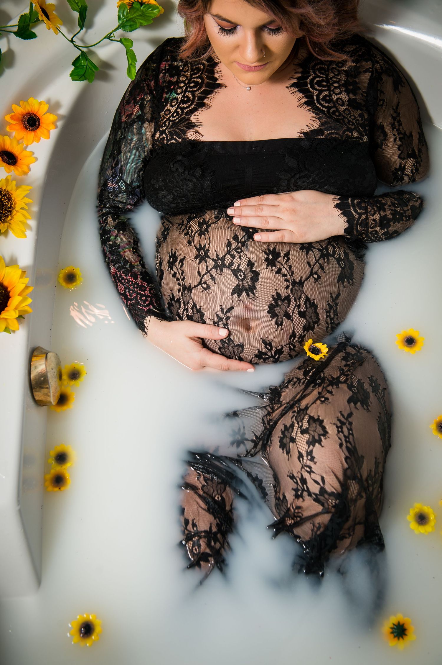 Maternity milk bath photo with black lace dress and vibrant sunflowers creating contrast.
