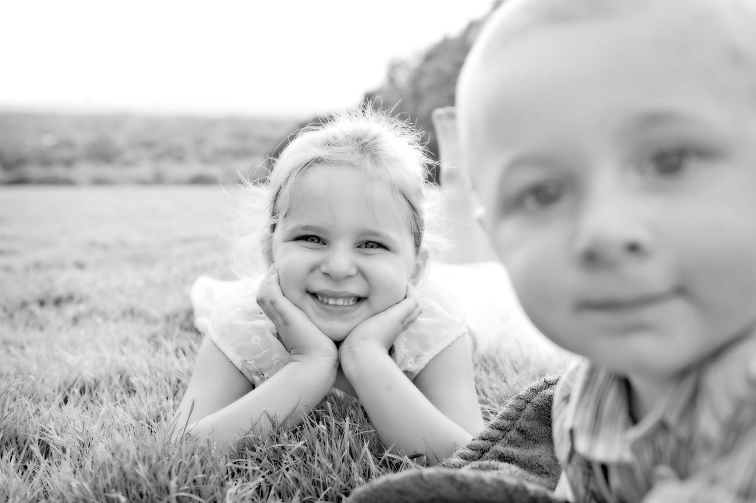 Black and white portrait of children laying in grass with natural lighting.