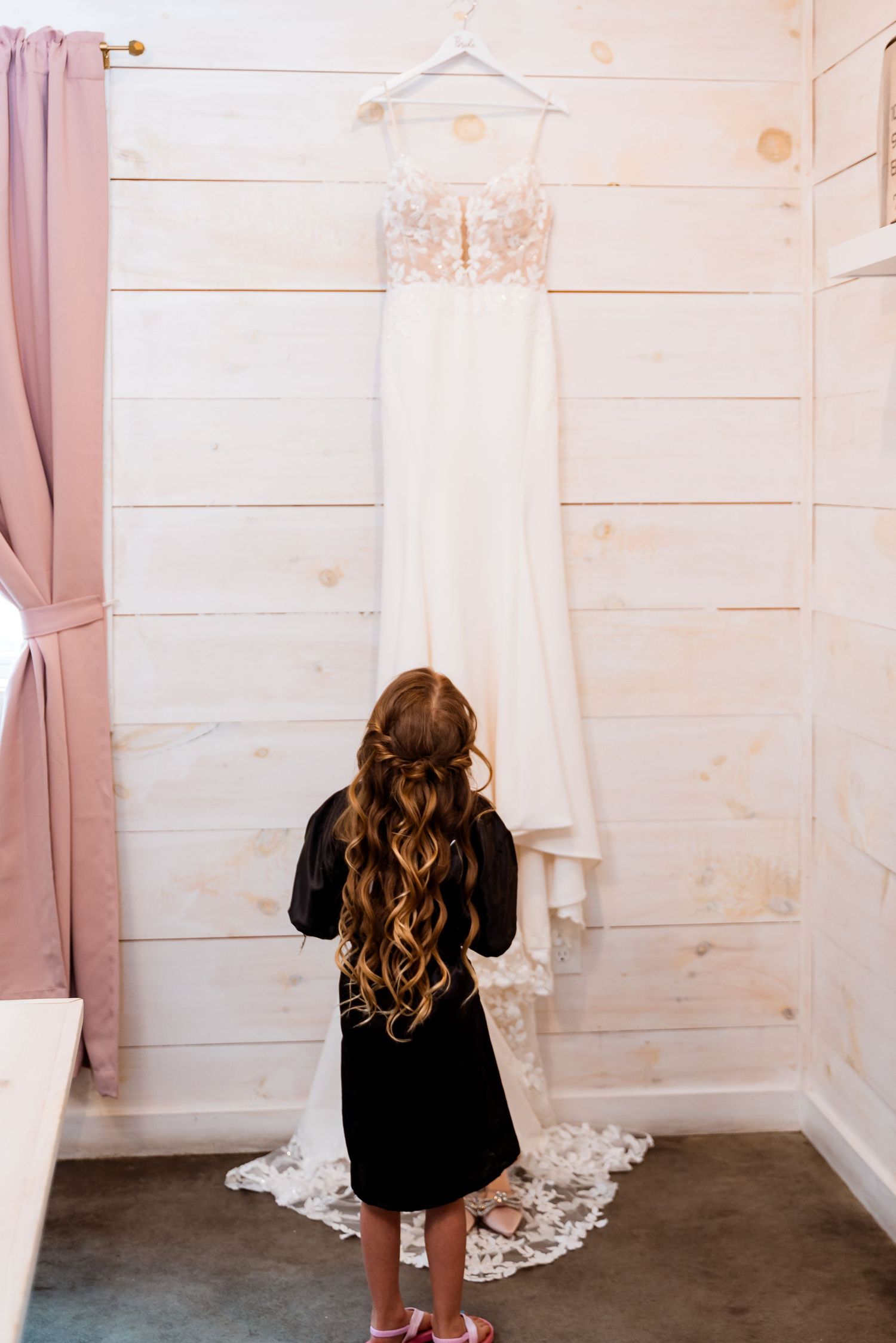 White wedding dress hanging on display against rustic wooden walls.
