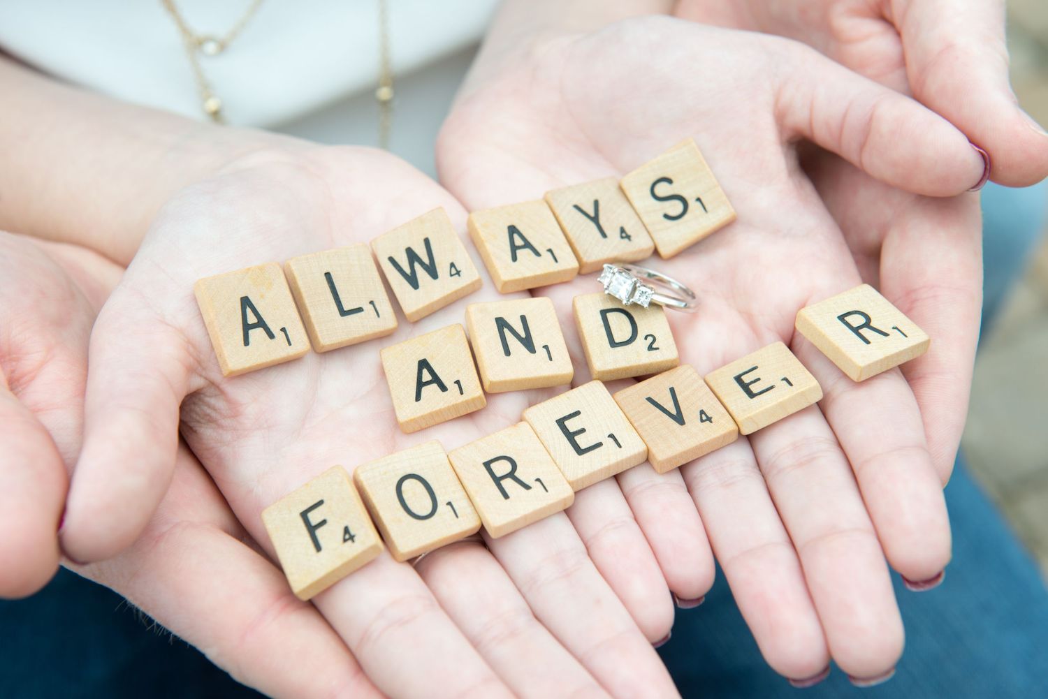 Hands holding Scrabble tiles spelling out 'Always and Forever'.