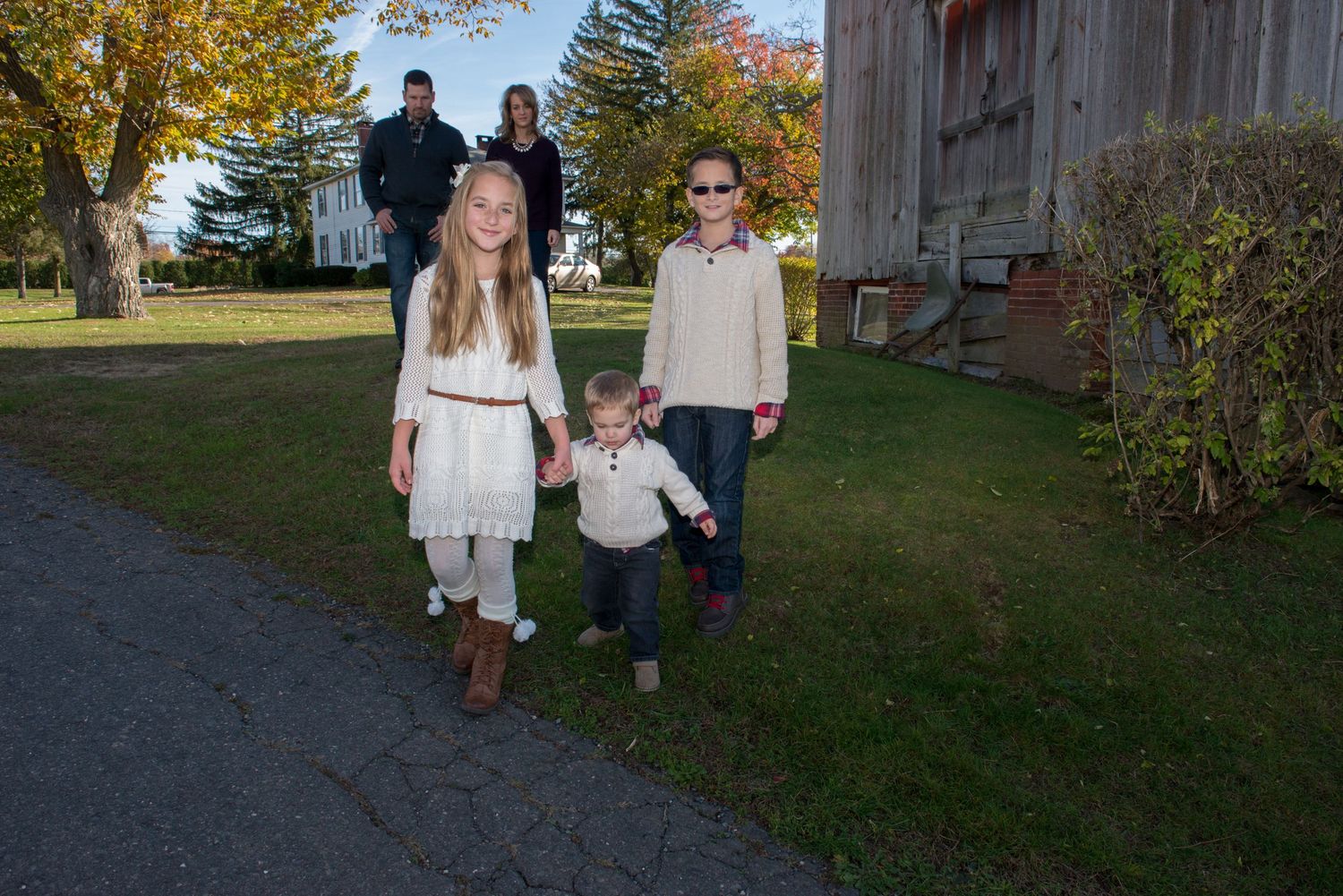 Family walking together on path during autumn with rustic barn in background.