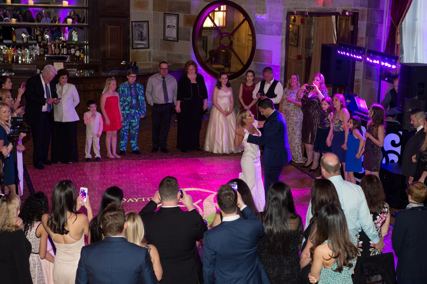 Wedding reception dance floor filled with guests under purple and pink lighting.