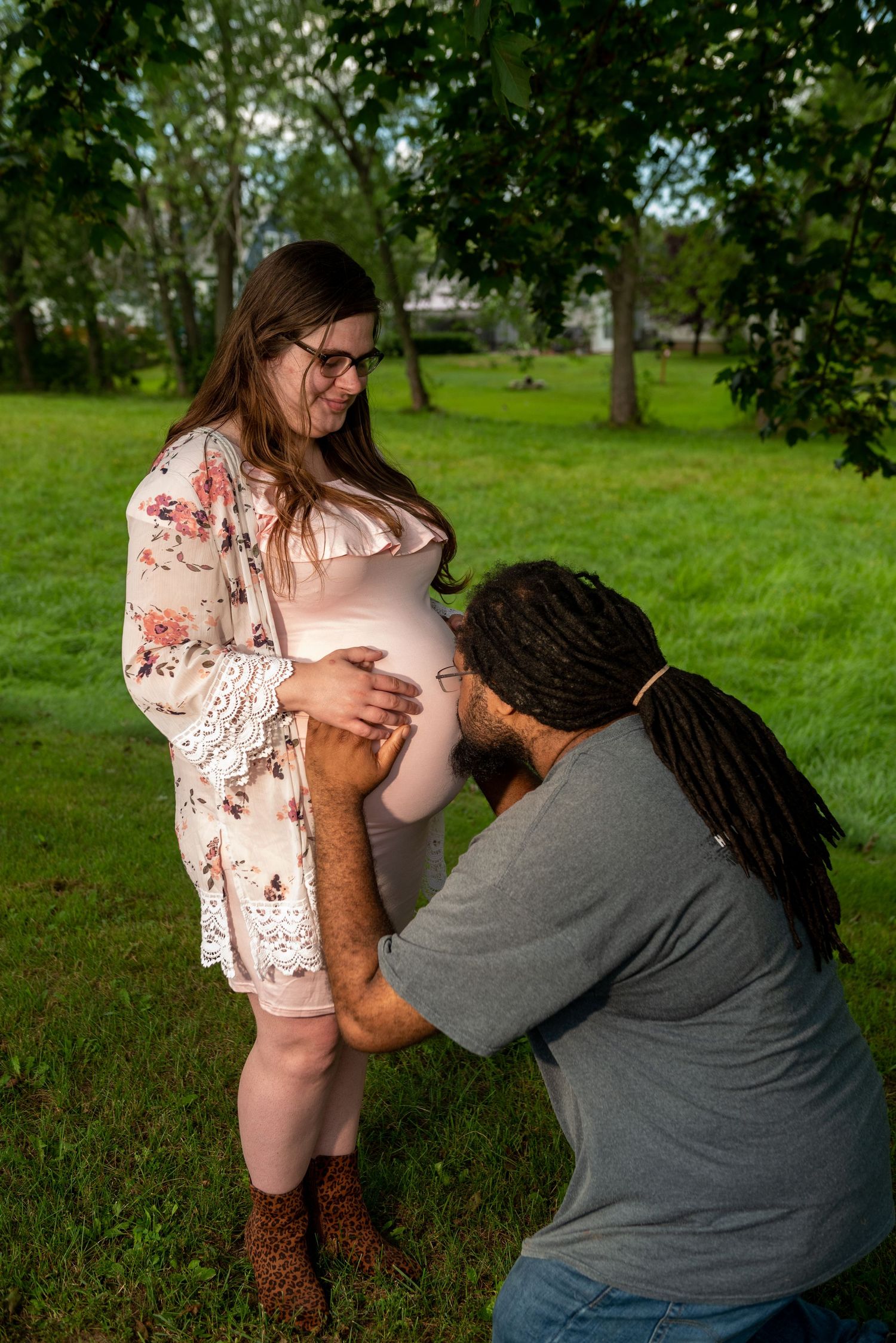 Intimate maternity photography session captured in a lush green outdoor setting.