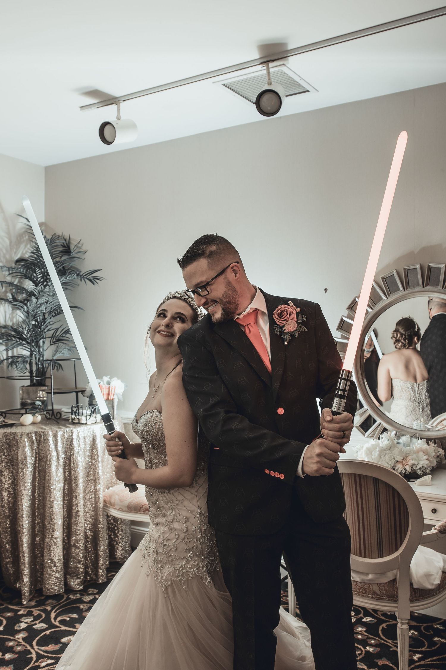Wedding couple posing with glowing lightsabers in an indoor reception setting.