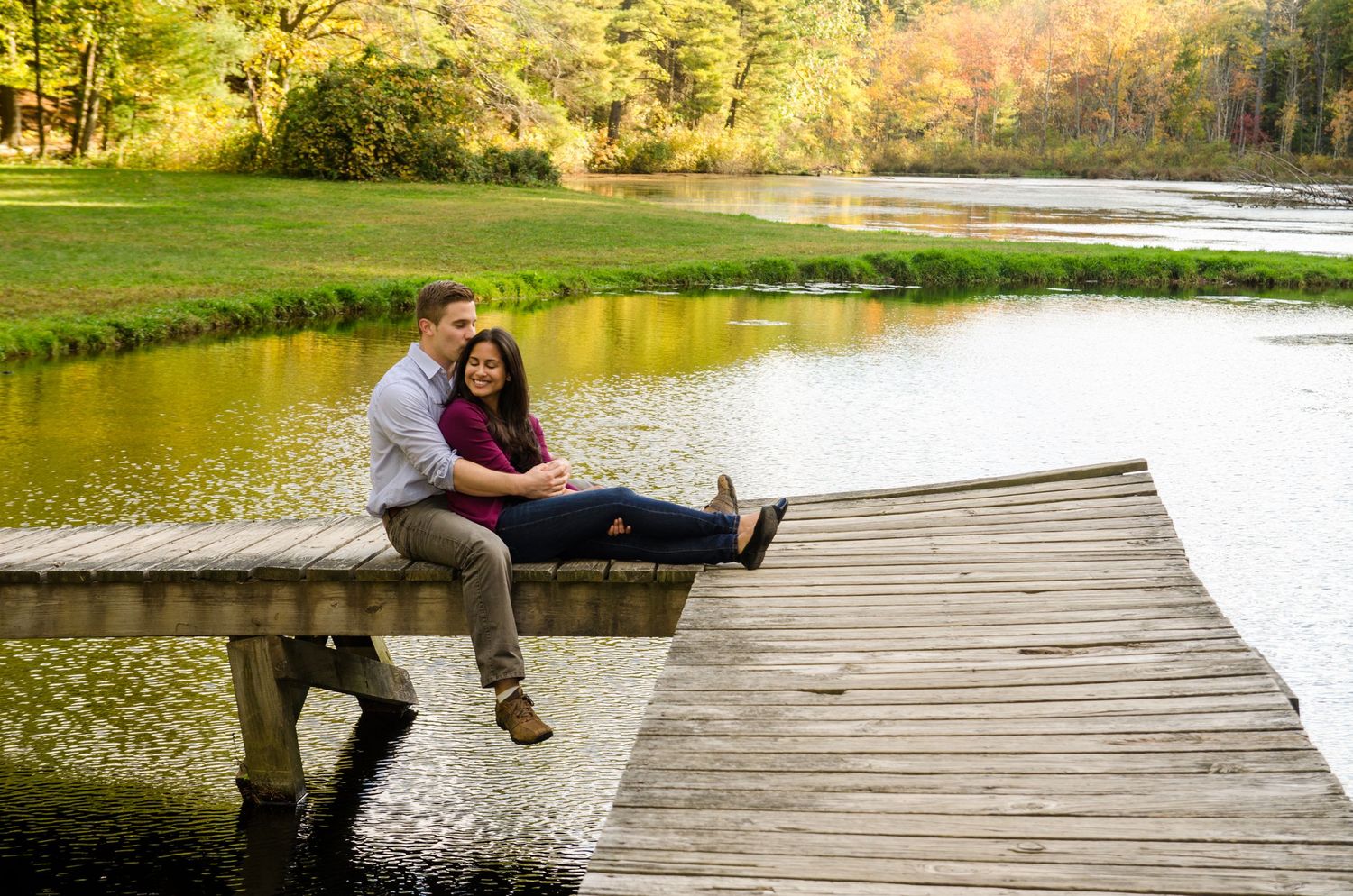 A couple sitting together on a wooden dock overlooking a peaceful lake.