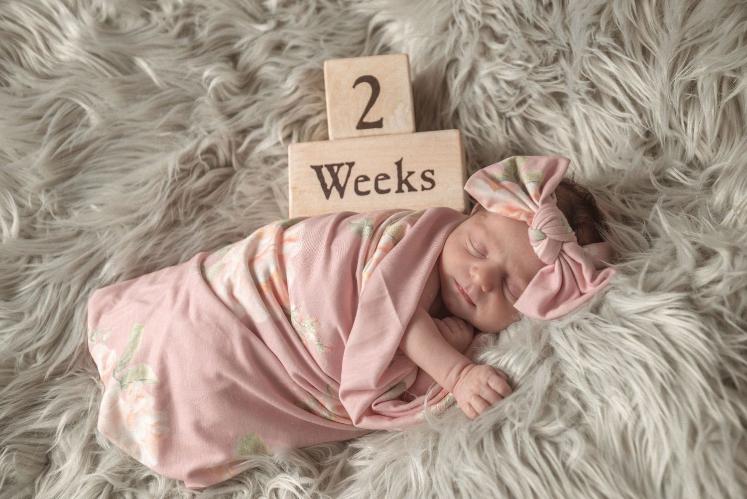 Weekly milestone photos of a sleeping newborn baby on soft white fur blanket.