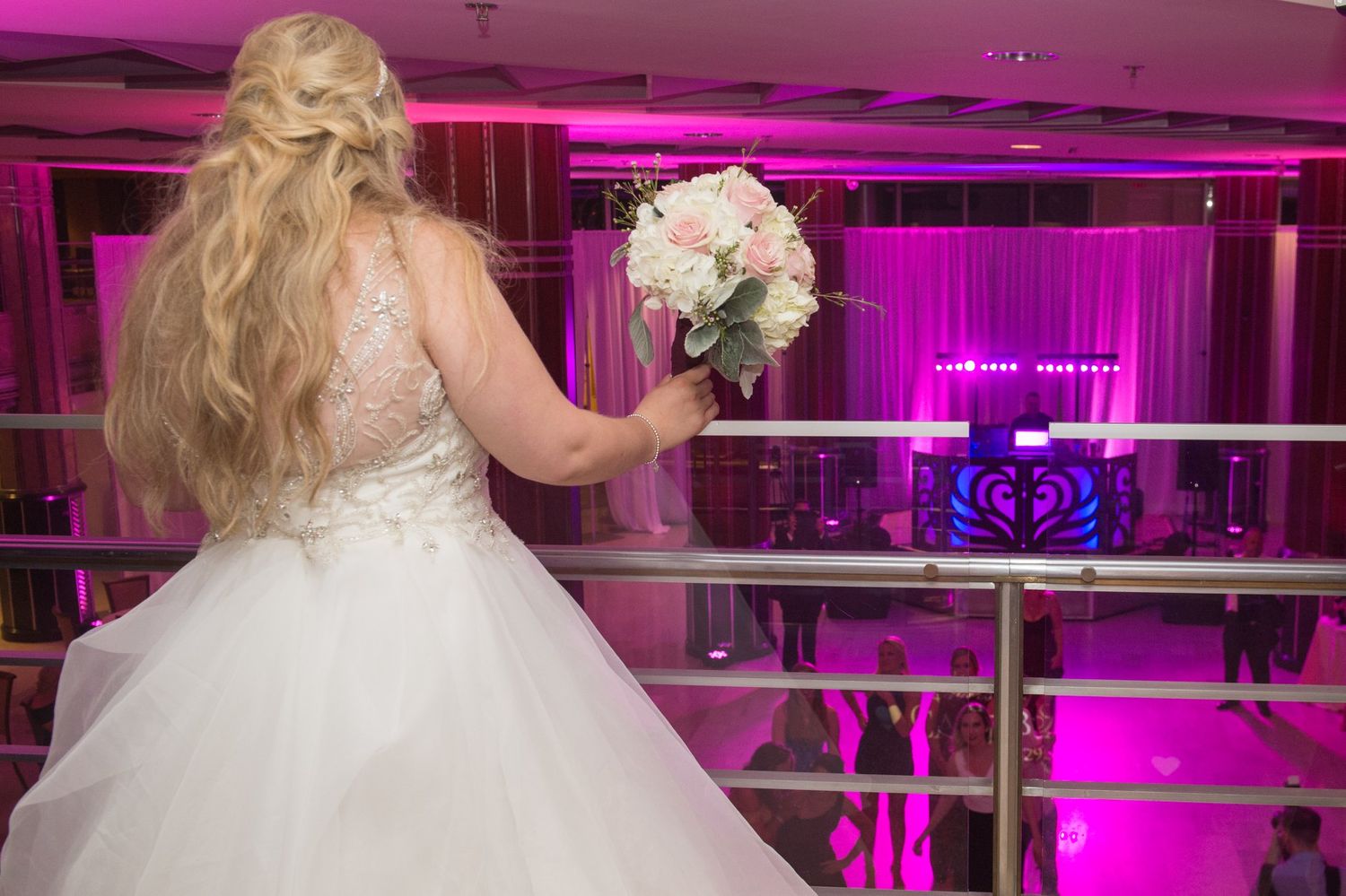 Wedding reception venue decorated in vibrant pink and purple lighting with elegant white decor.
