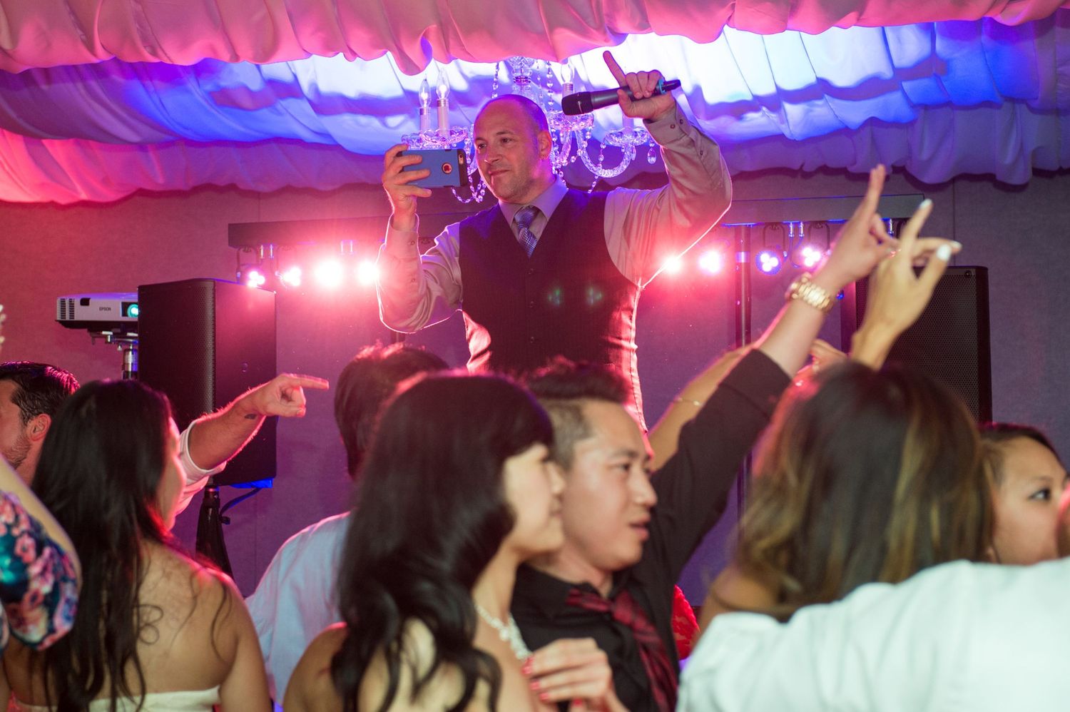 A lively wedding reception dance party with colorful lighting and raised hands in celebration.