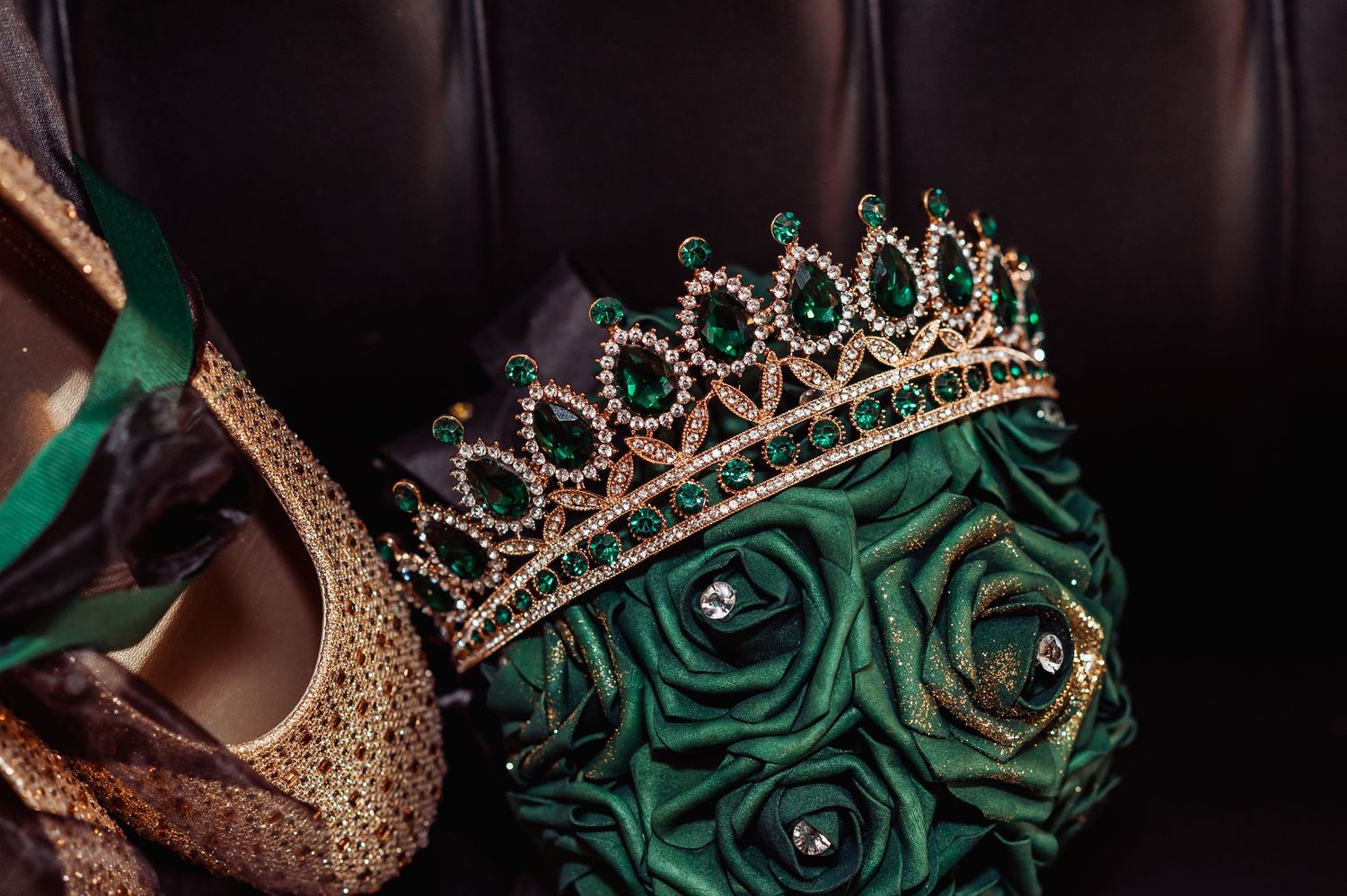 Close-up details of an emerald green gown with gold crown and crystal embellishments.