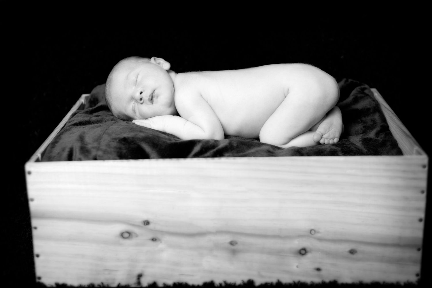 Black and white artistic portrait of a sleeping newborn in a wooden drawer.