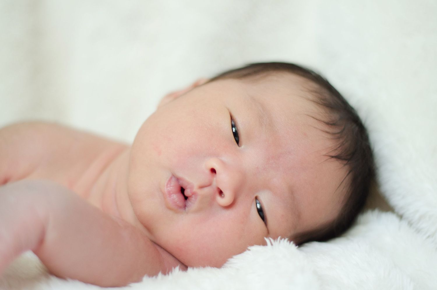Gentle close-up of a sleeping newborn on white bedding.