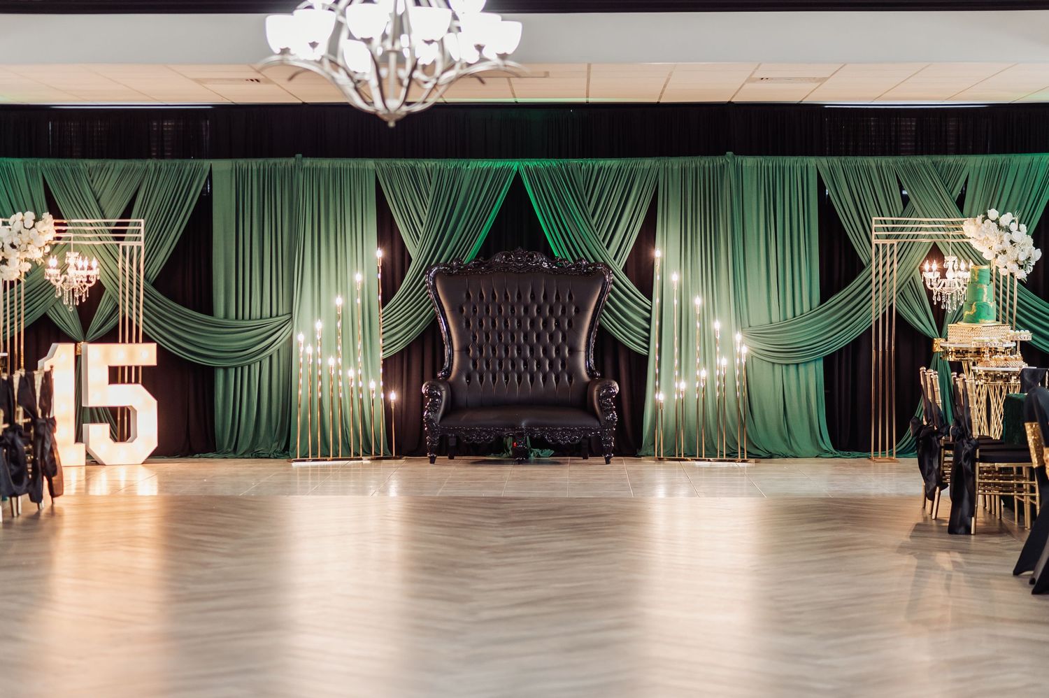 Empty elegant ballroom with green drapes and chandeliers set up for special event.