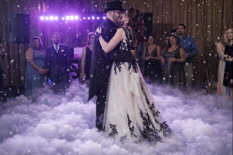 Dancing couple surrounded by purple lighting and fog effects at a wedding reception celebration.