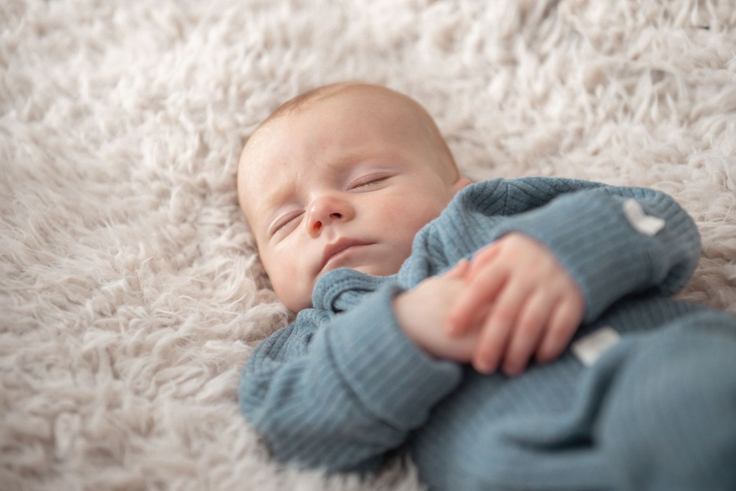 Newborn baby sleeping peacefully in cozy blue outfit on white fluffy blanket.