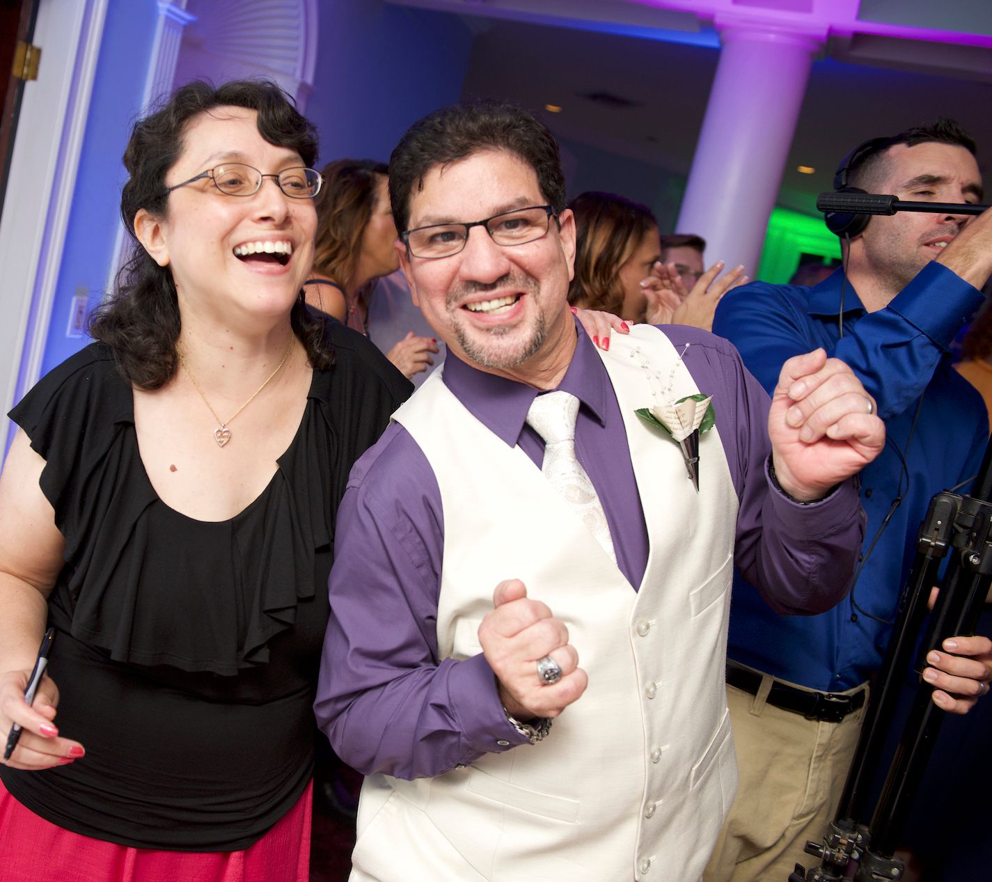 People dancing and laughing together at a party with purple lighting.