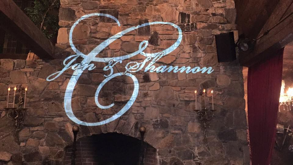 Elegant monogram projection on rustic brick wall with candlelight accents.