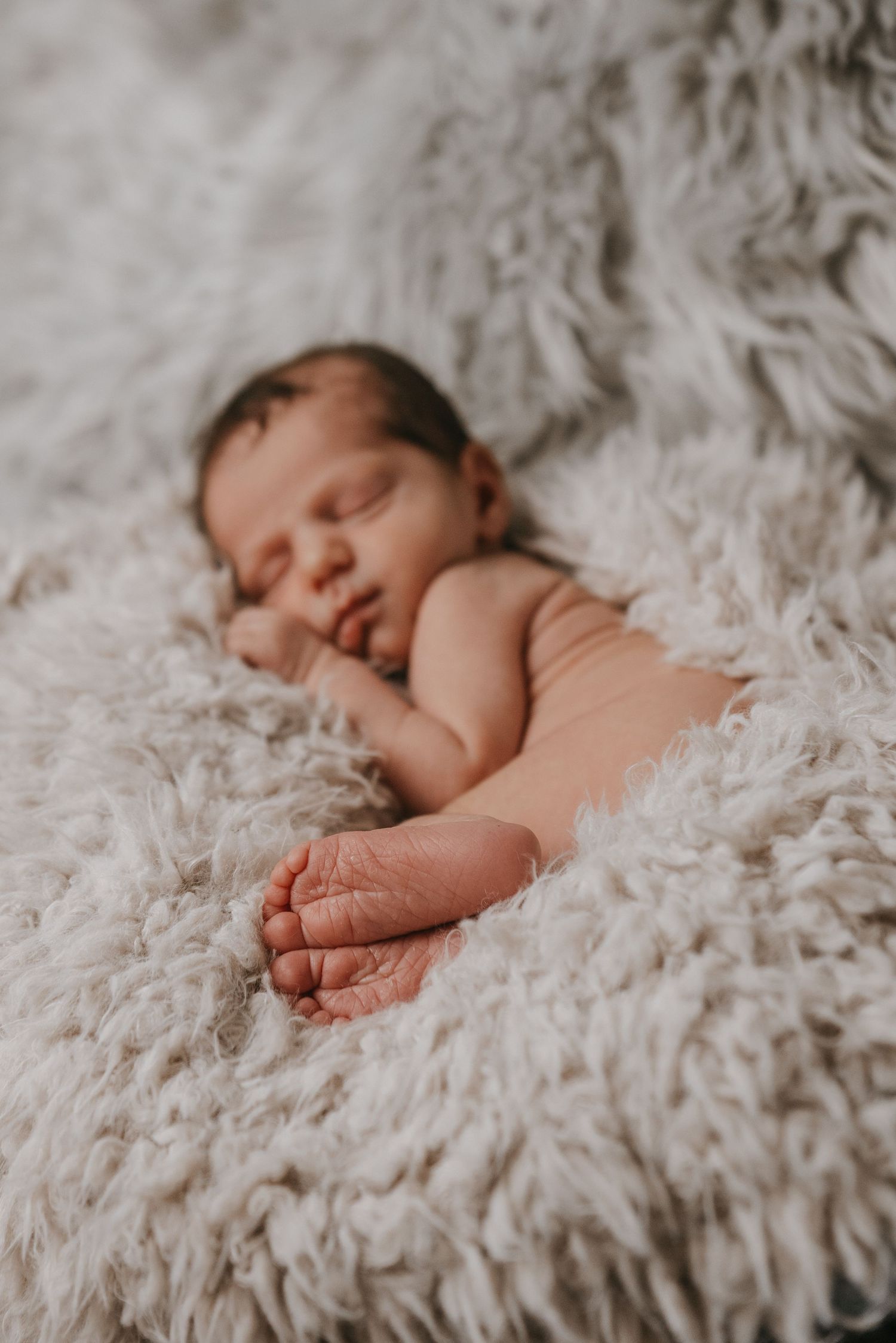 Sleeping newborn baby nestled in soft white fluffy blanket.