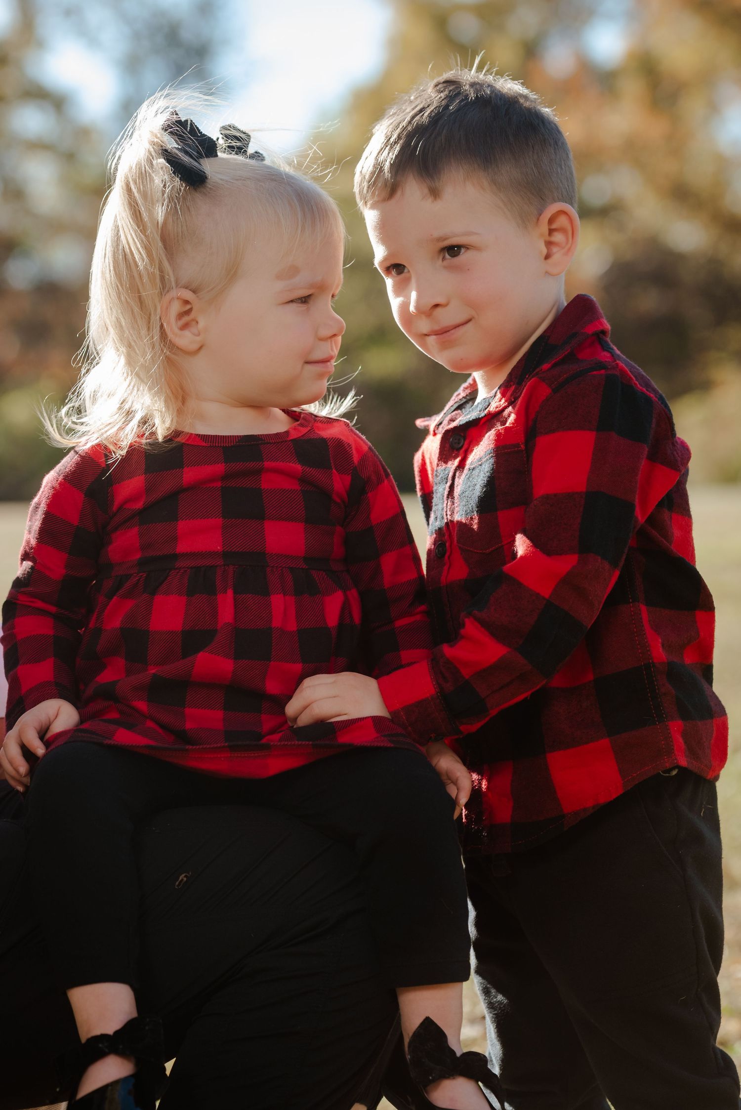 Two young children in matching buffalo plaid shirts playing together outdoors.