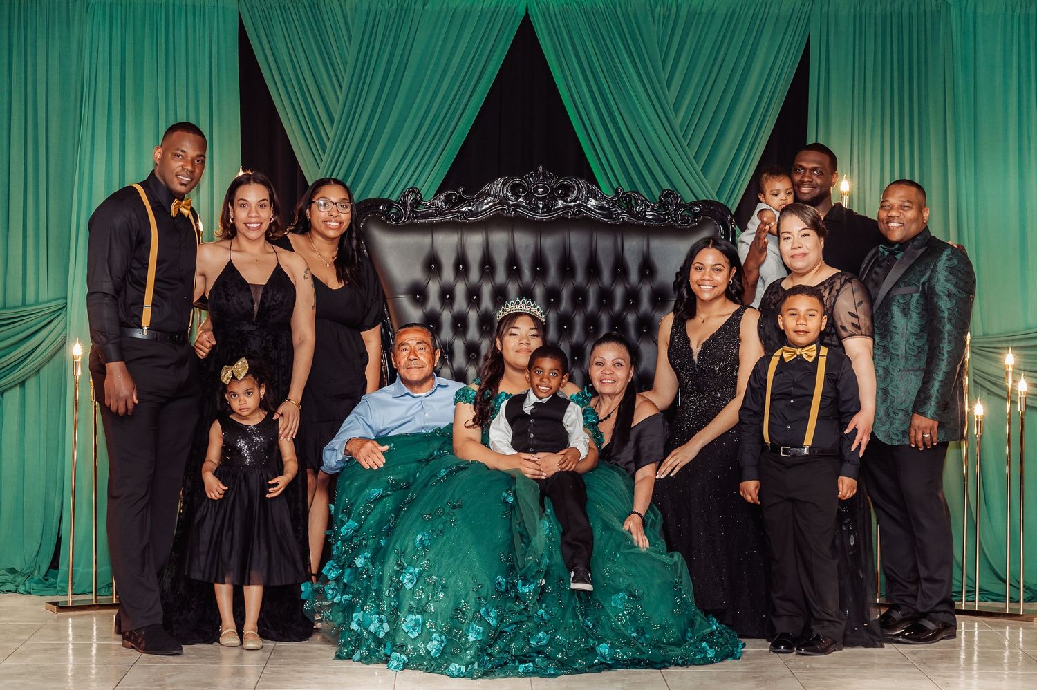 Wedding party dressed in black attire poses with emerald green accents in formal setting.