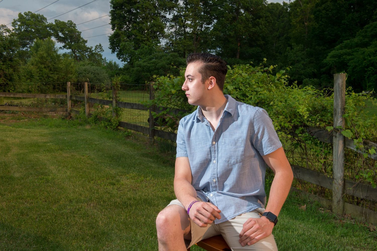 Person relaxing in casual attire on wooden bench in lush garden setting.