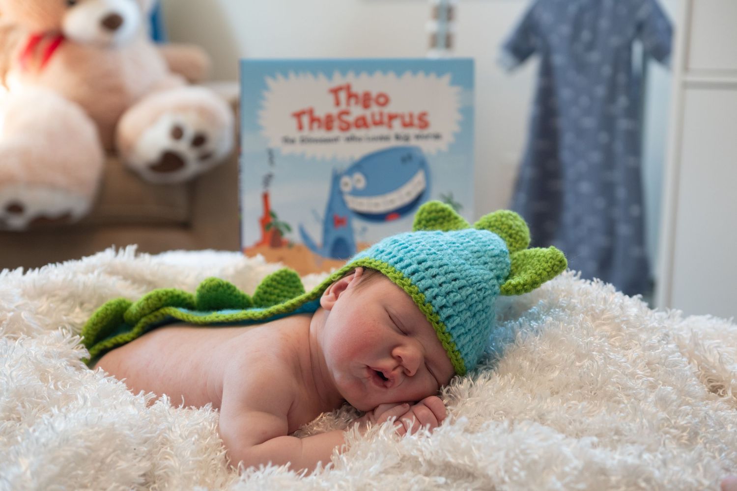 Infant sleeping on white blanket with stuffed animals and children's books nearby.