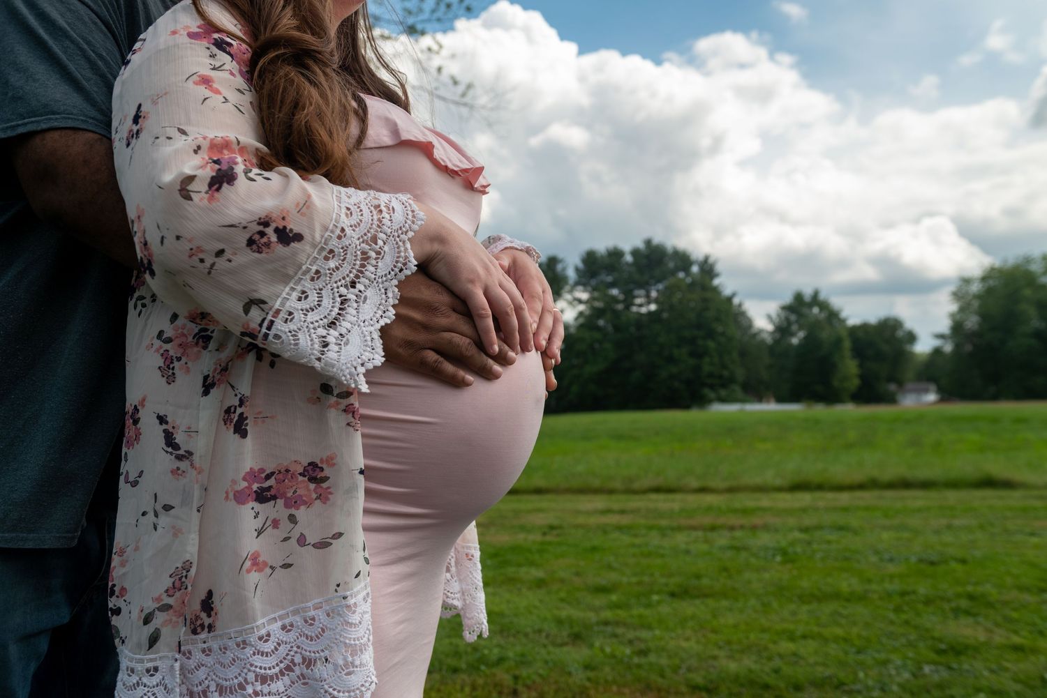 Maternity photos taken outdoors in a grassy field on a cloudy day.