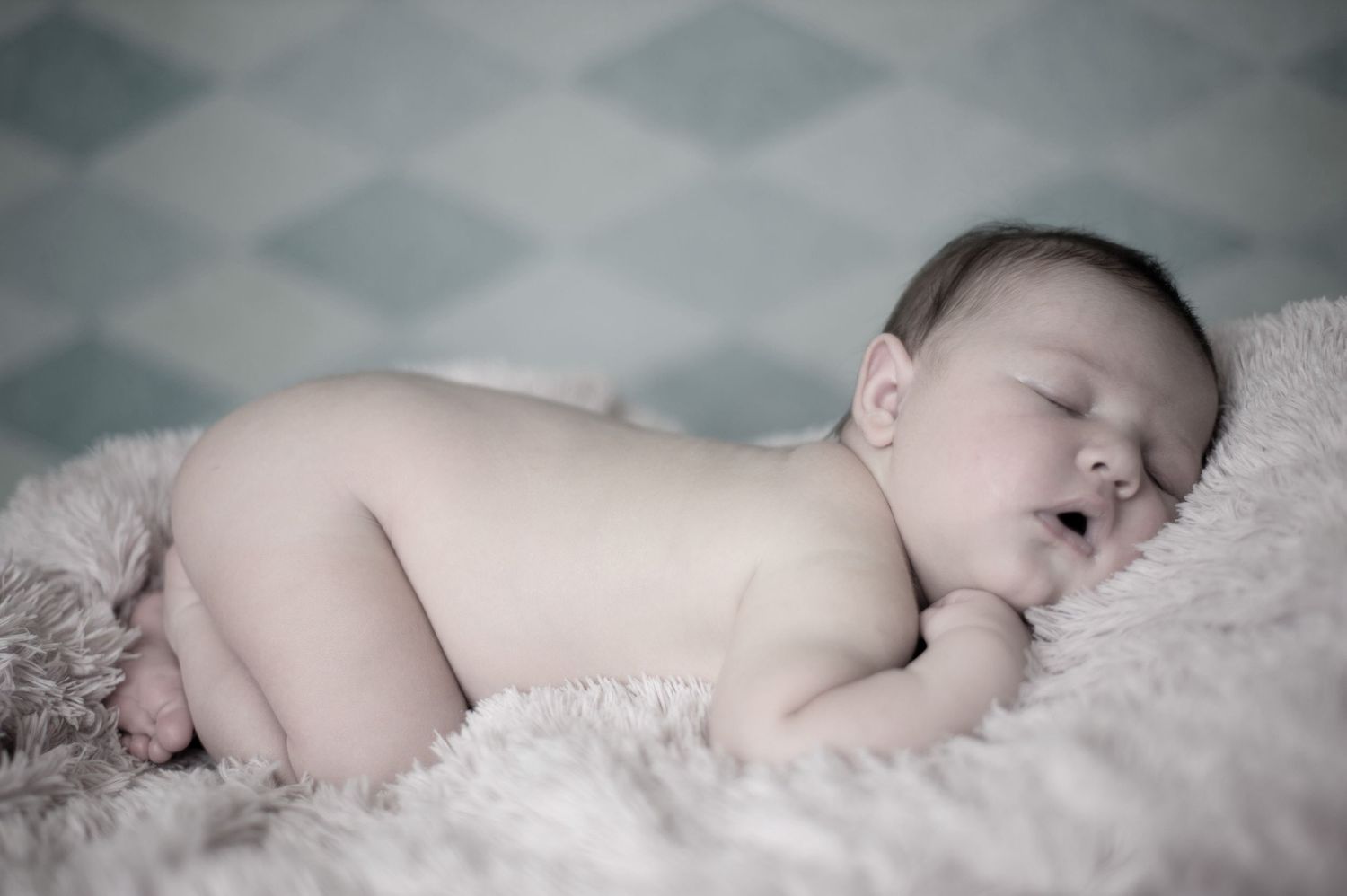 Peaceful newborn resting on soft white bedding in muted tones.
