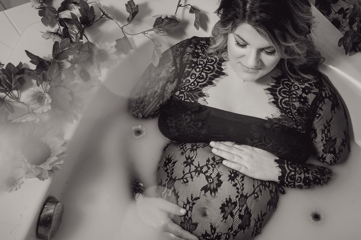Artistic milk bath portrait with scattered flowers and delicate lace details.
