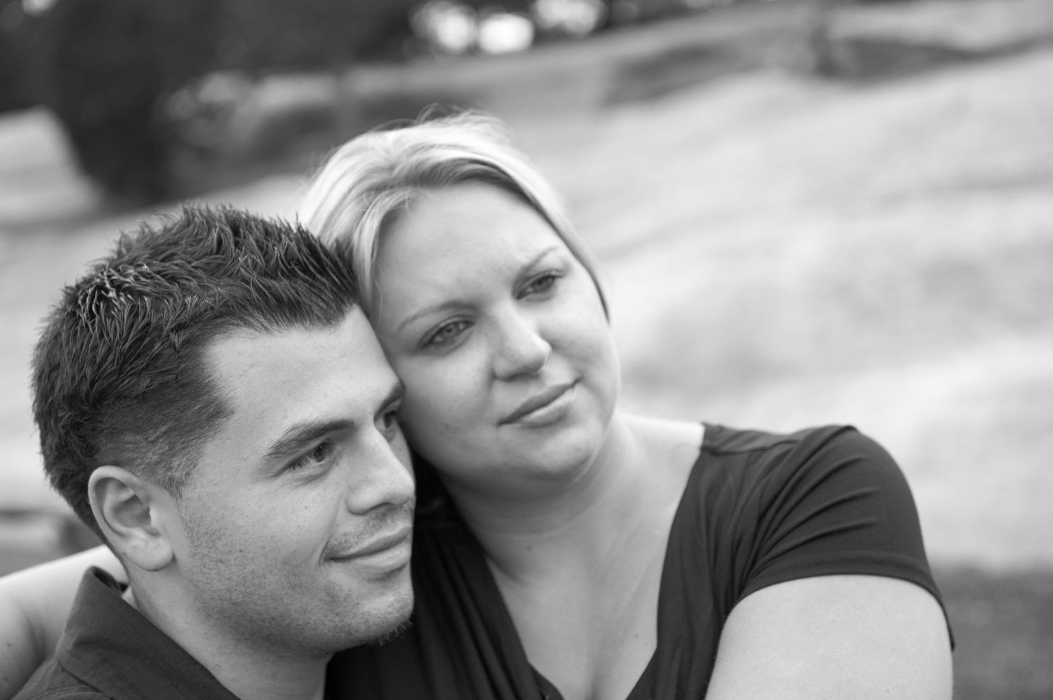 A black and white close-up portrait of a couple sharing an intimate moment outdoors.
