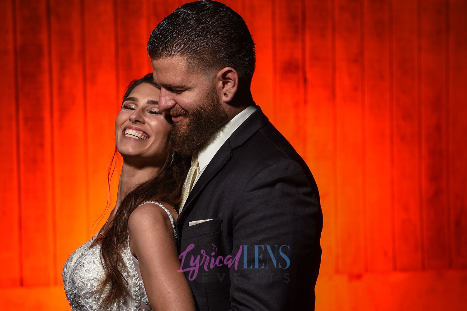 Wedding couple embracing against dramatic red backdrop lighting.