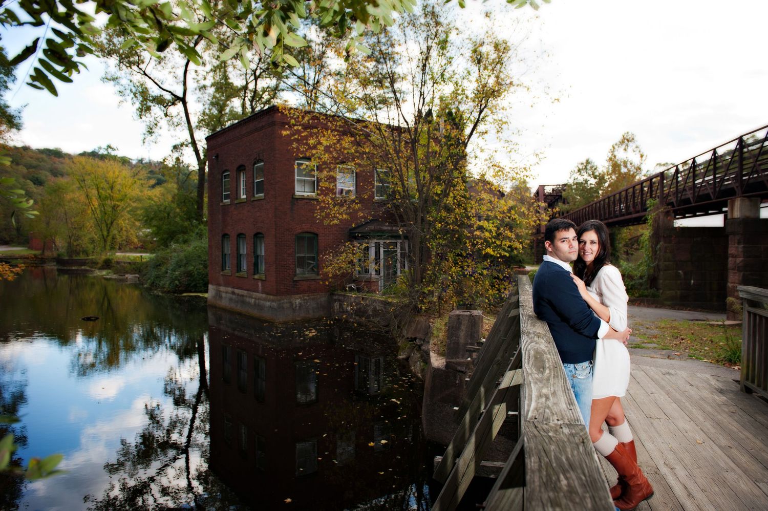 A couple shares an intimate moment on a wooden deck overlooking a serene lake during autumn.