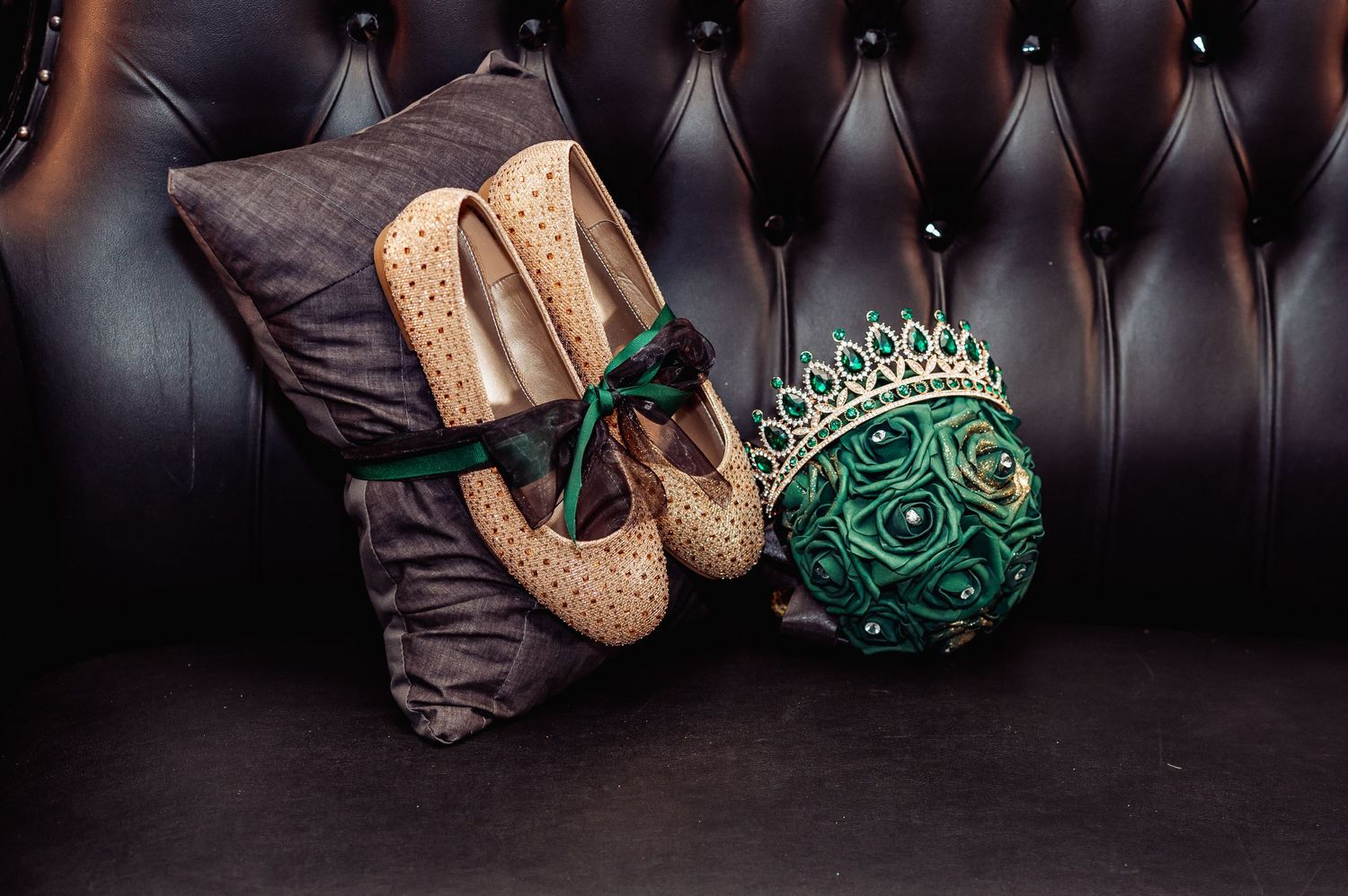 Elegant arrangement of emerald green accessories and gold glitter shoes against dark leather.