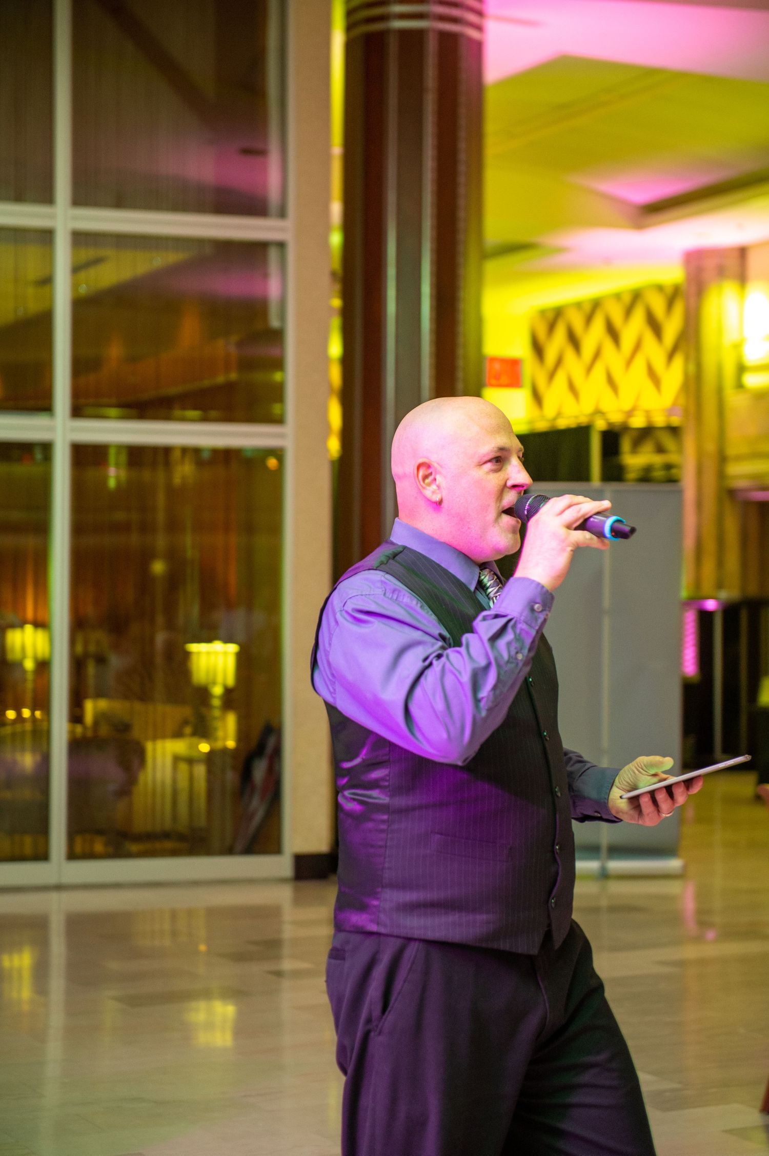 Entertainment performer in formal attire singing into microphone at wedding reception.