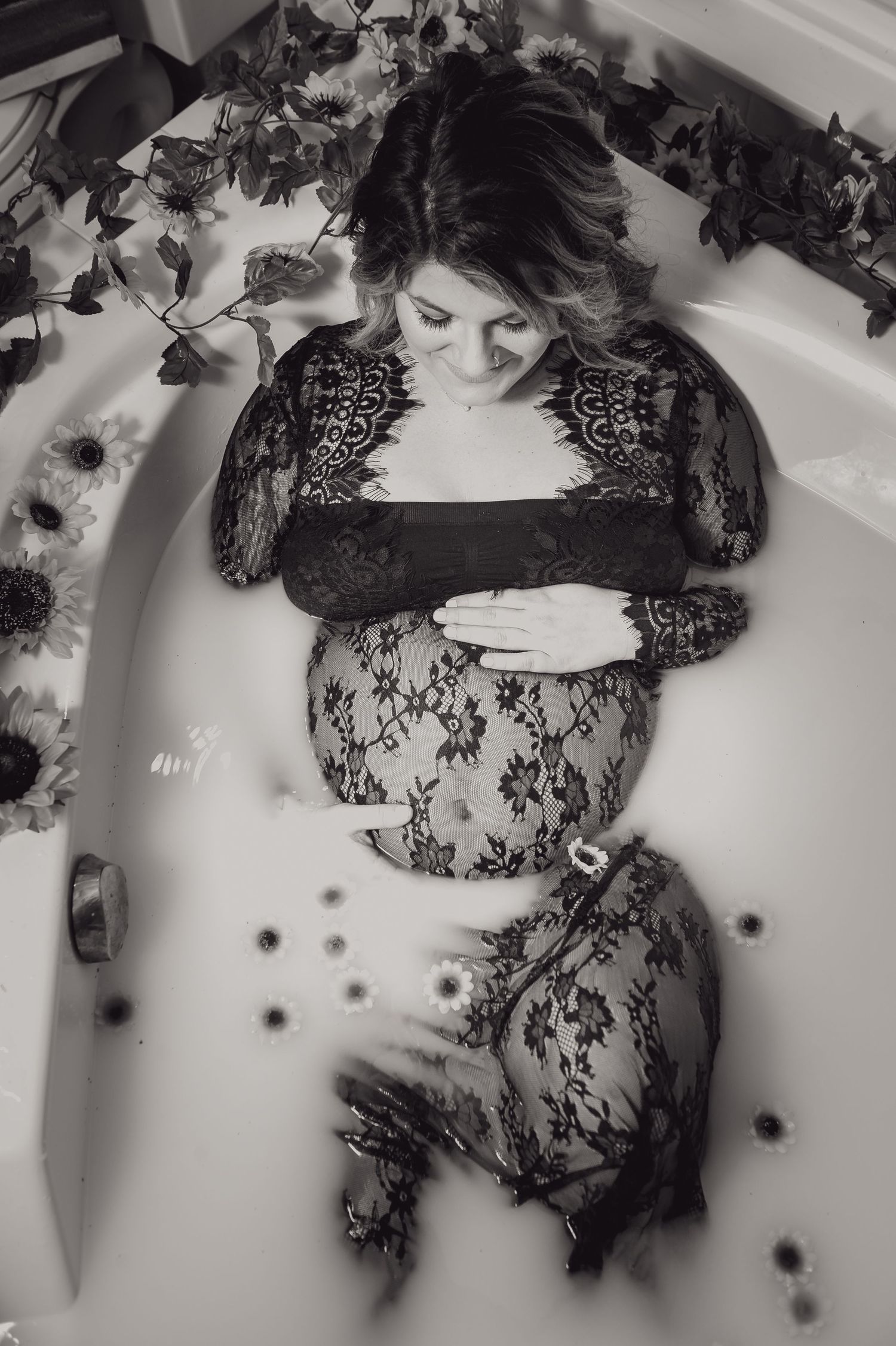 High-angle view of a milk bath session with scattered flowers and lace details.