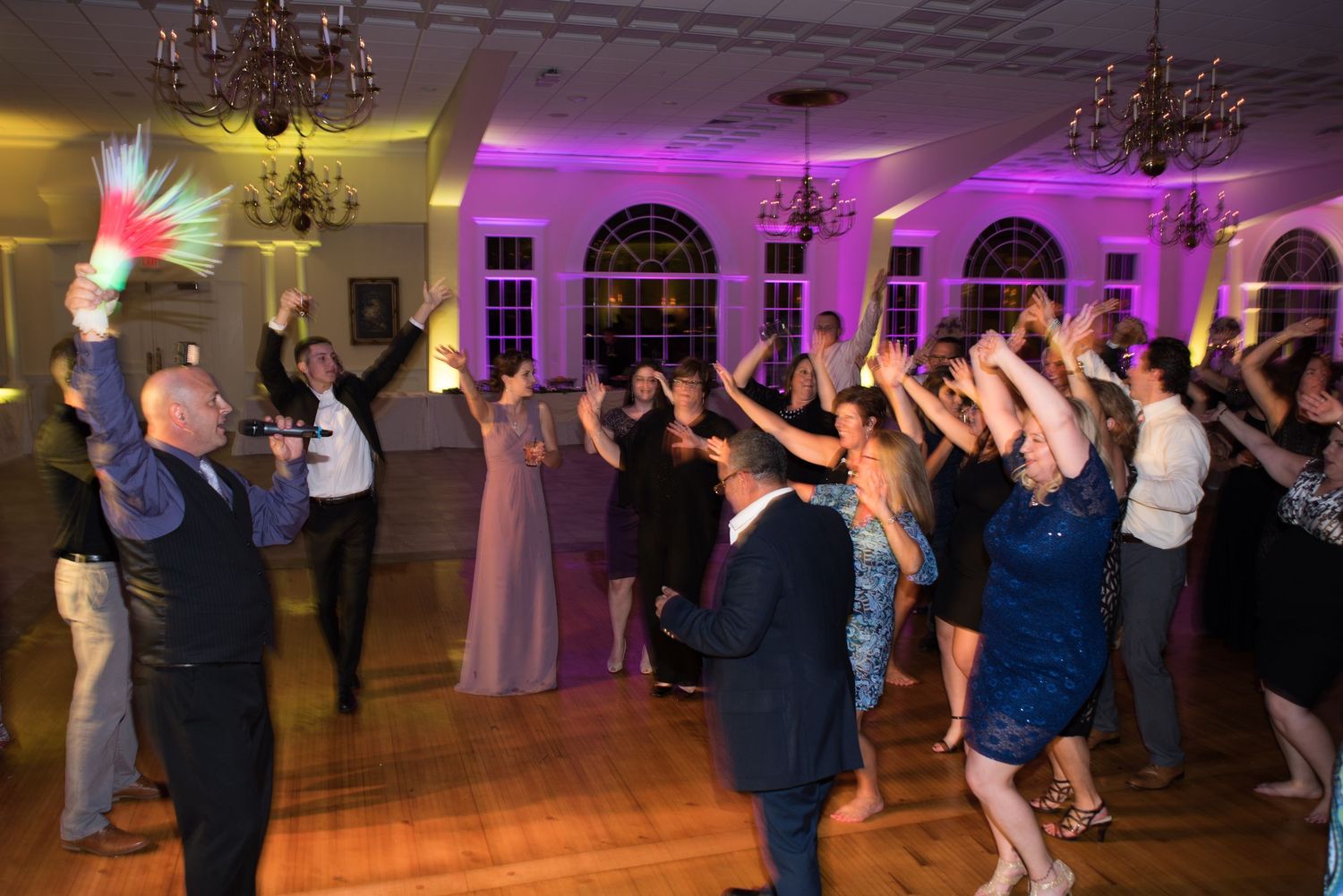 Wedding guests dancing and celebrating on the reception dance floor with colorful lighting effects.