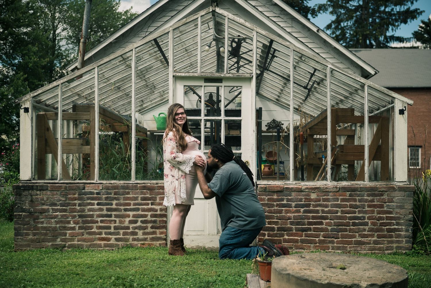 Maternity photos taken outside a rustic greenhouse with brick and white painted wood.