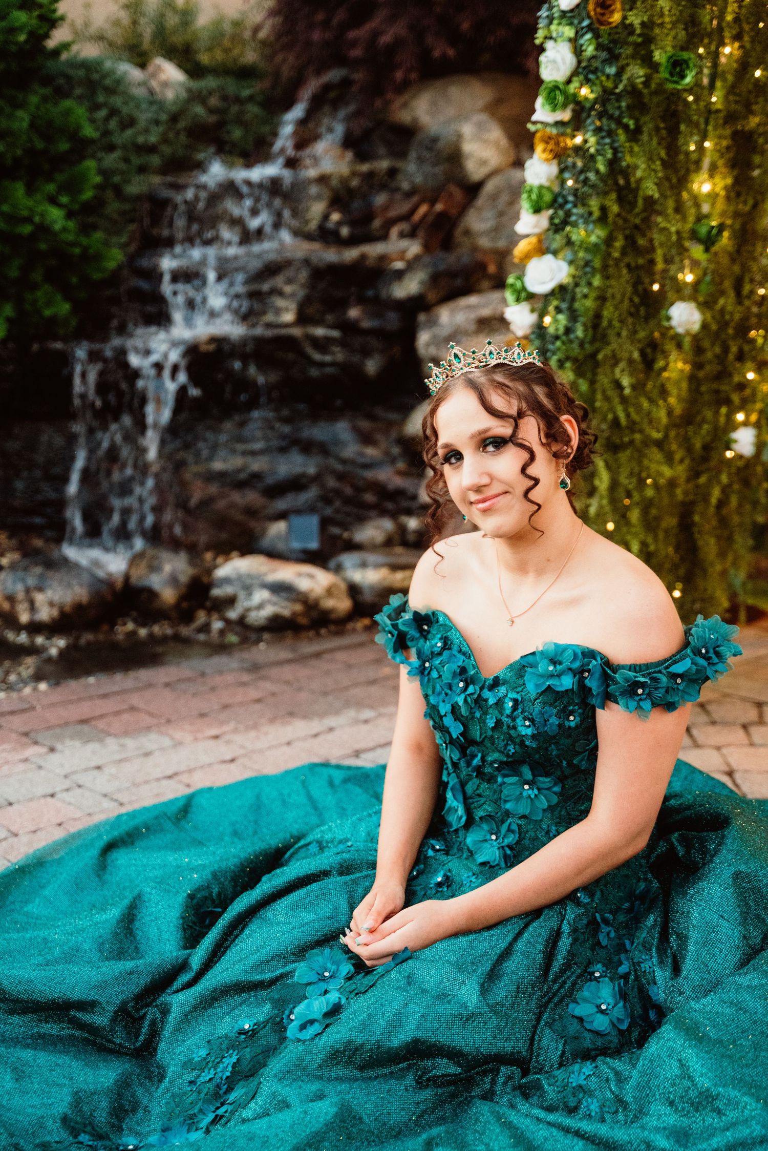 Elegant teal ball gown photographed near a garden waterfall.
