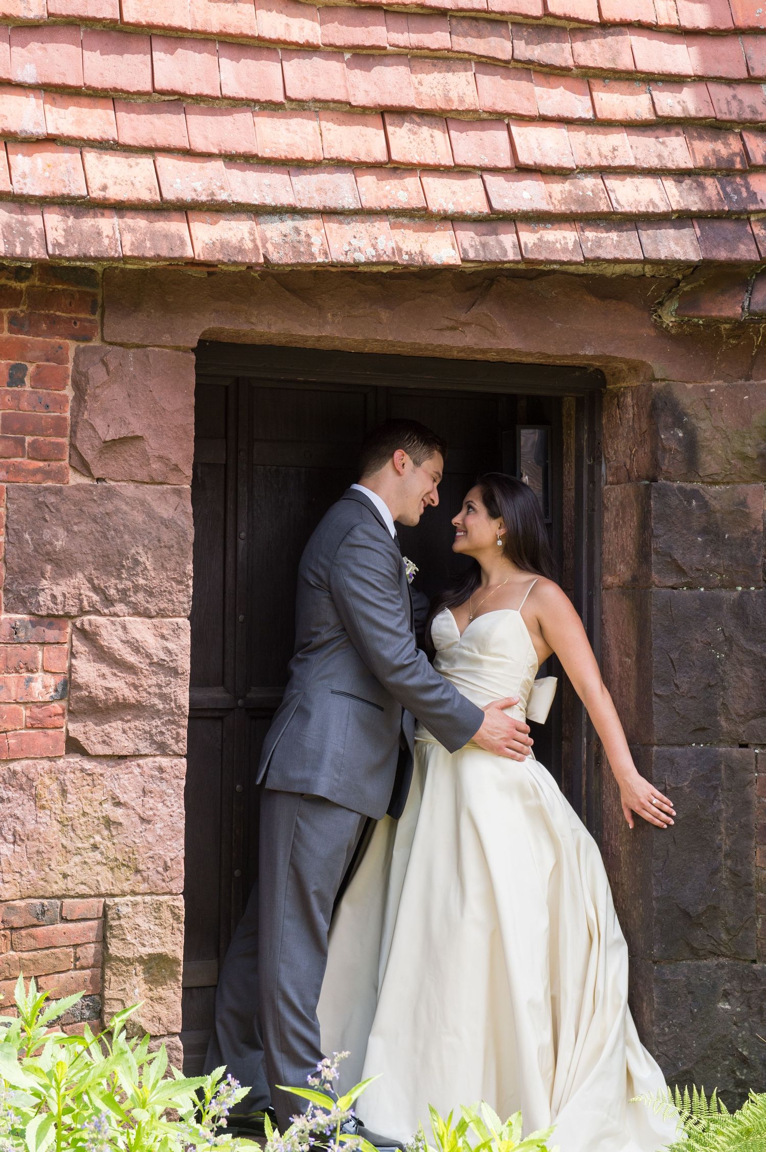 Couple shares intimate moment under stone archway during wedding photoshoot.