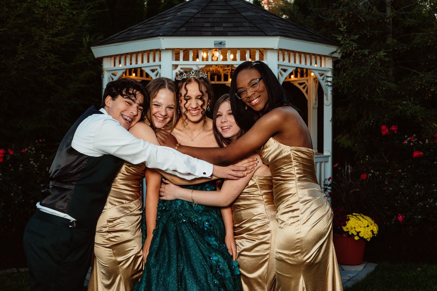 Wedding party members in teal dresses and formal attire pose together on outdoor garden bench.