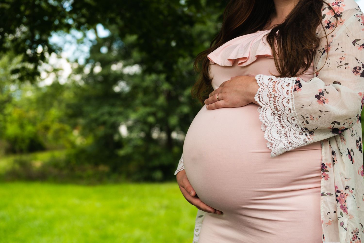 Maternity photoshoot in a lush green garden setting with soft natural lighting.