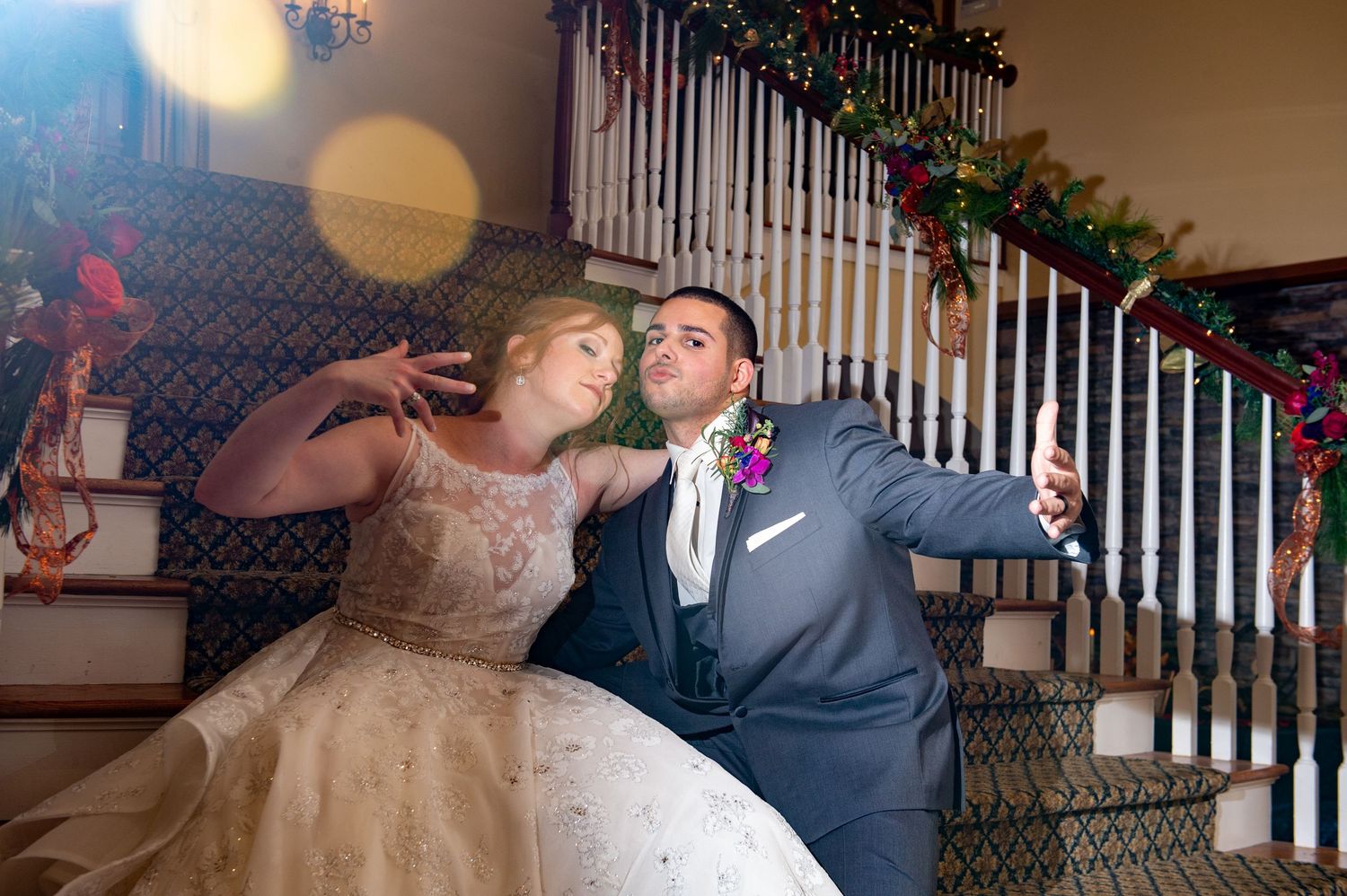 A couple in wedding attire share a playful moment on decorated stairs during their reception celebration.