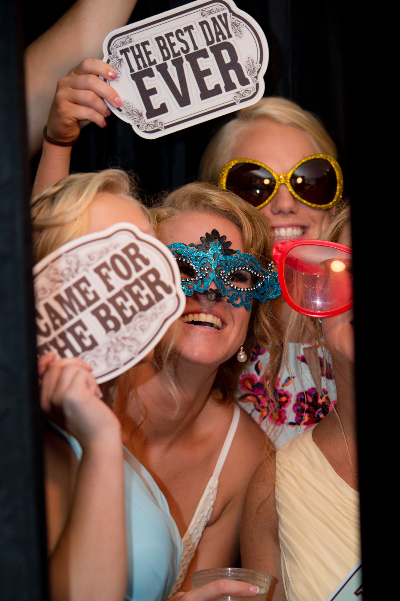 Party guests posing with fun photo booth props and signs at wedding celebration.
