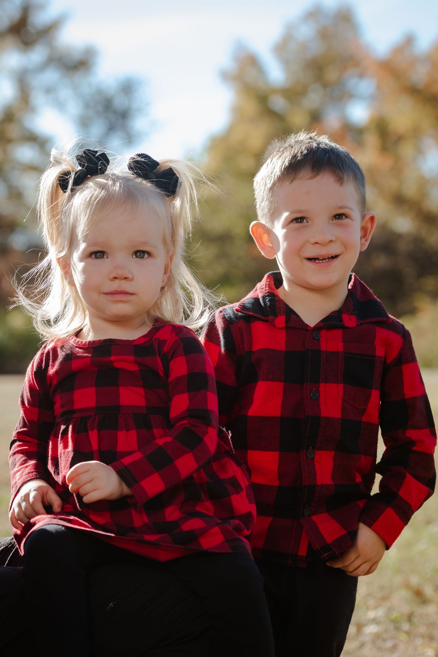 Two children wearing matching red and black buffalo plaid shirts pose together outdoors.