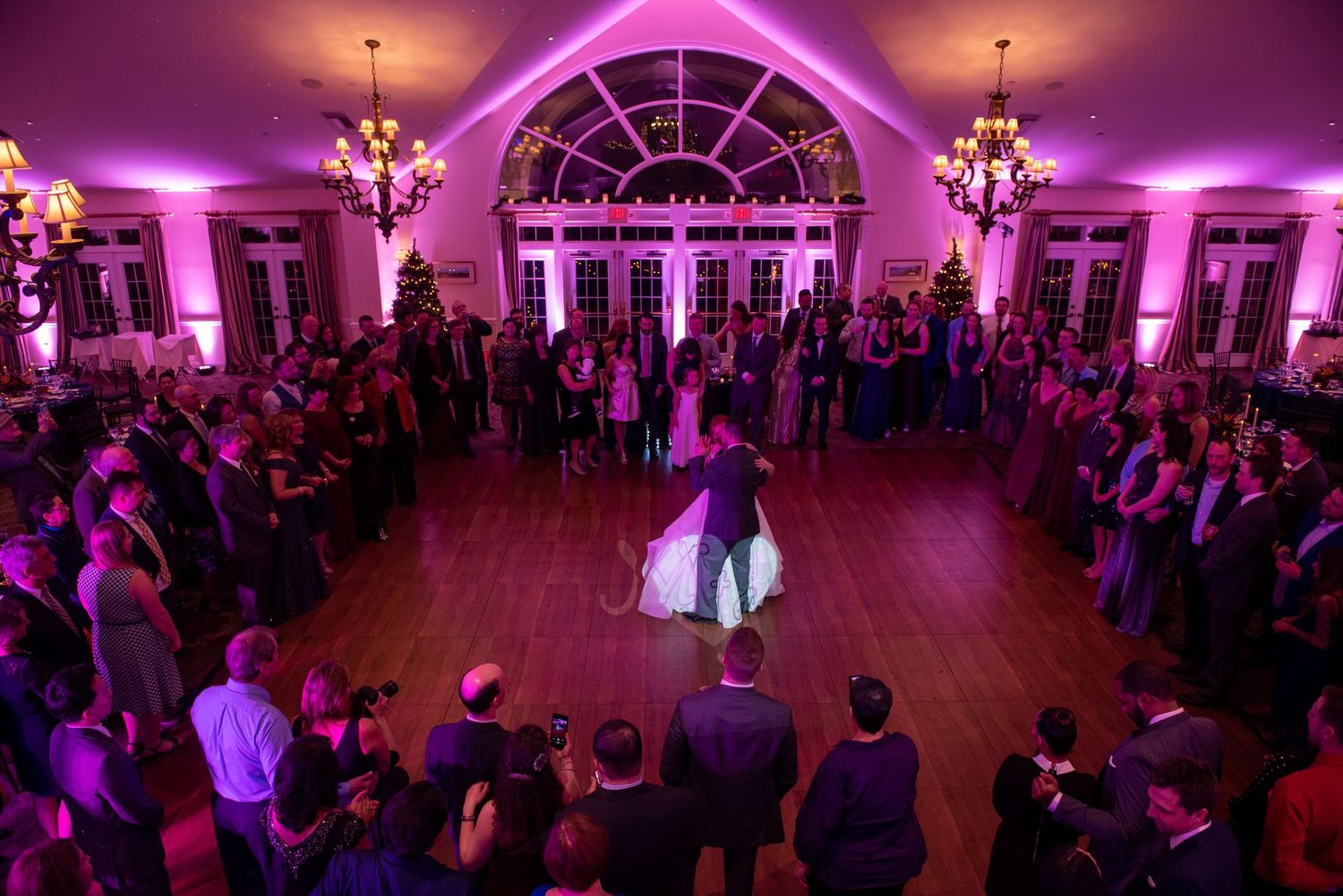 Grand ballroom with purple uplighting and arched windows filled with dancing party guests.