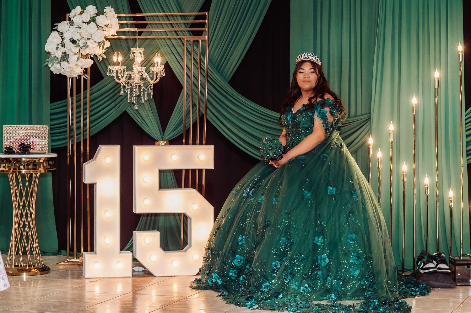 Elegant quinceañera celebration with emerald green draping and chandelier lighting.